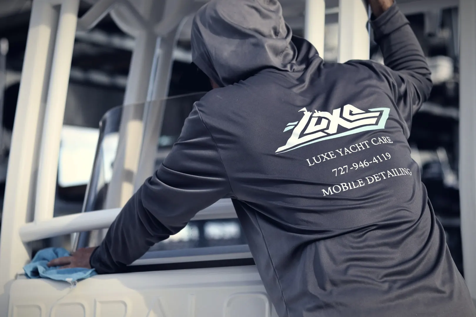 Wiping down a center console with a blue towel, in a Luxe Yacht Care shirt that reads Mobile Detailing